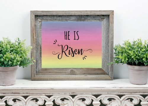 He is Risen Free Easter Printable shown in a rustic wood frame