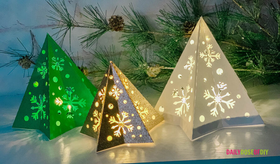 3d tree lanterns made from cardstock paper.  One is white, one is gree, one is gold glitter with snowflakes cut out of them 