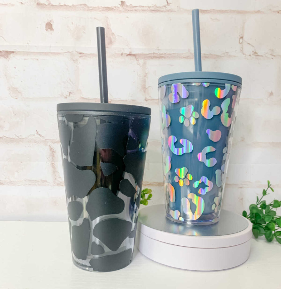 TWO TAPERED TUMBLERS ONE BLACK TUMBLER WRAPPED WITH BLACK VINYL IN COW PRINT DESIGNS.  One blue tapered tumbler wrapped in hollographic vinyl with cheetah and paw print designs. 