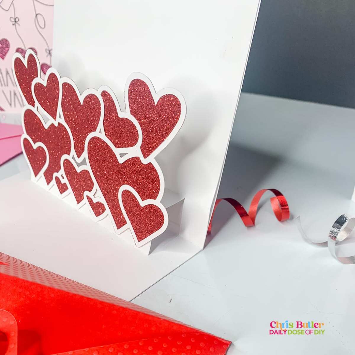 Picture of the inside of a heart pop up card with red glitter hearts outlined in white 
