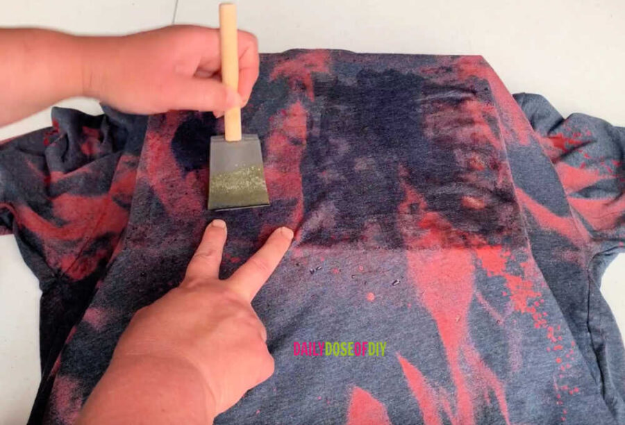Using a brush to apply bleach to a shirt getting it ready for a sublimation design.