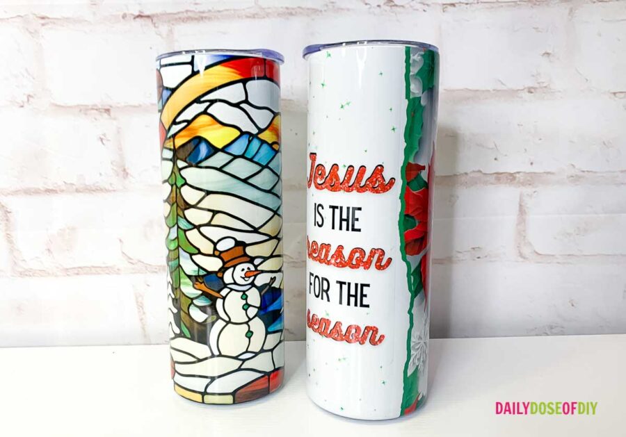 two sublimated tumblers one with a stained glass snowman scene in multiple colors and one with poinsettia design that says "Jesus is the reason for the season" 